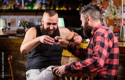 Drunk conversation. Cheers concept. Hipster brutal bearded man drinking alcohol with friend at bar counter. Men relaxing at pub. Strong alcohol drinks. Friday relax in pub. Friends relaxing in pub