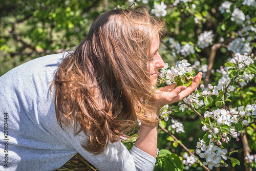 Beautiful woman smelling flowers among spring blossoming trees