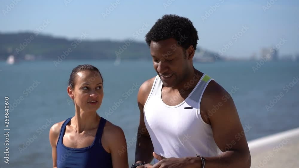 Multiethnic couple in sportswear jogging along embankment. Happy sporty young couple running together and talking at riverside at sunny day, slow motion. Workout concept Multiethnic couple in sportswear jogging along embankment. Happy sporty young couple running together and talking at riverside at sunny day, slow motion. Workout concept