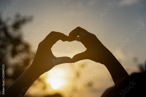 human hands in heart shape framing in sunset