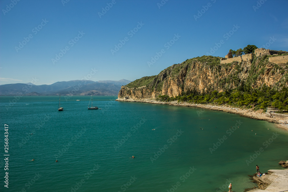summer vacation and travel concept photography of Mediterranean sea bay scenery landscape with castle on top of mountain along waterfront shoreline and cruise boats on water surface 
