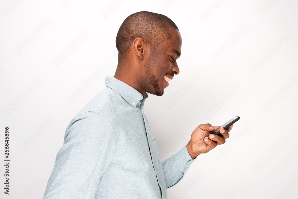 Profile of happy young black man looking at cellphone by white background Profile of happy young black man looking at cellphone by white background
