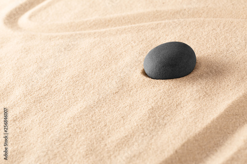 Black basalt zen meditation stone in a Japanese sand garden. Minimalism to focus concentration on spiritual healing. An alternative therapy in spa wellness resort. Sand background with copy space.