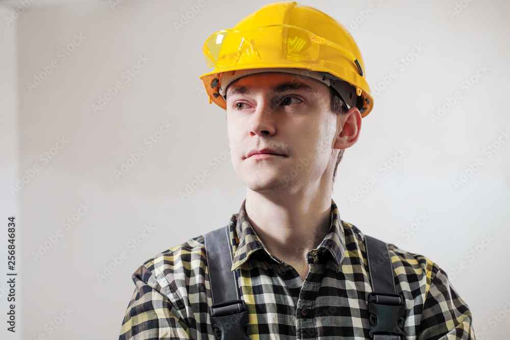 Portrait of a young male builder and repairman in a yellow helmet against the background of a wall. Portrait of a young male builder and repairman in a yellow helmet against the background of a wall.
