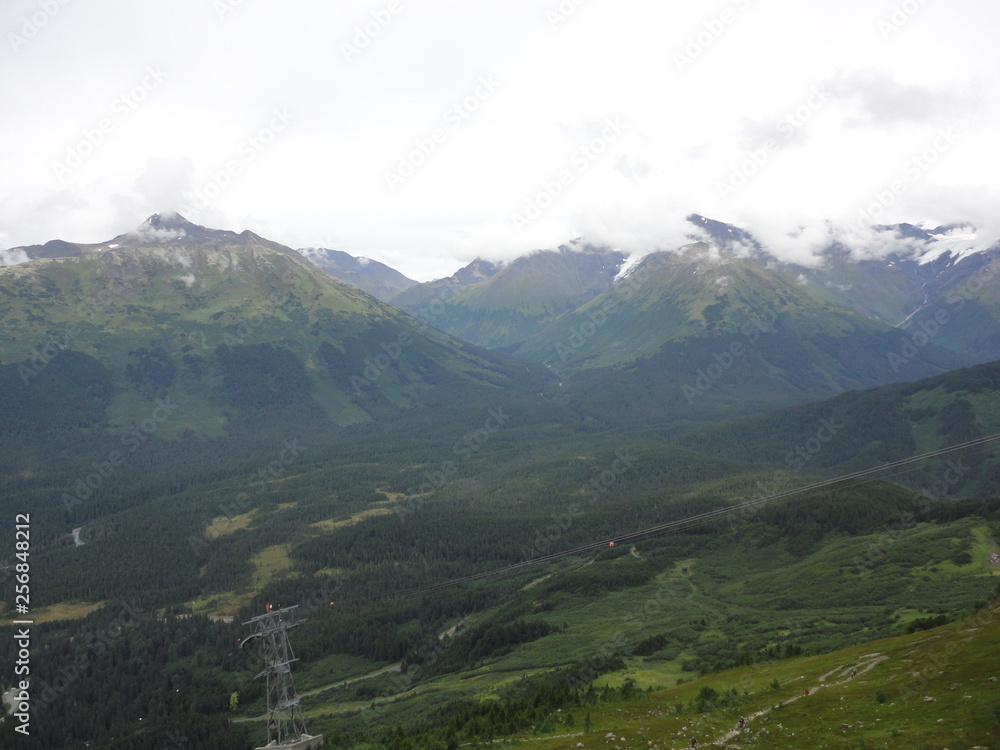 View from atop a mountain in the wilderness of Alaska. Peaks and ocean stretching off into the sky and clouds
