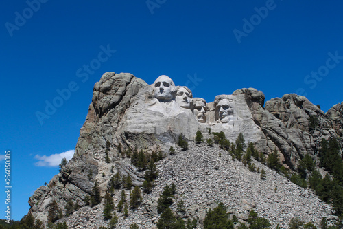 Mount Rushmore on a clear summer day with no clouds, a bright blue sky and rocks in the foreground. © Joni