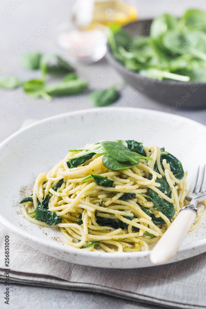 Spaghetti pasta with spinach and green pesto, in a white plate on gray stone background