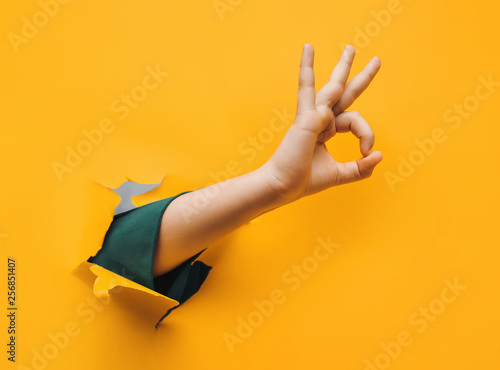 Hand OK sign. The teenage hand came out into the hole of yellow paper and shows symbol of Okay. Copy space, fine. photo