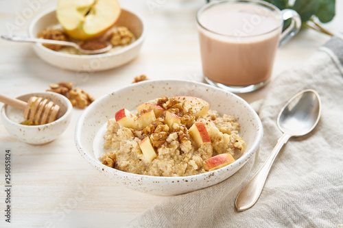 Oatmeal with apple, walnuts and cup of cocoa on white wooden light background. Side view. Healthy diet breakfast