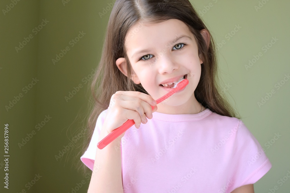 Caucasian beautiful girl brushing her teeth. Long haired smiling white girl brushing teeth with pink toothbrush on green background. Green eyed cute child in pink tshirt doing her morning hygiene. Caucasian beautiful girl brushing her teeth. Long haired smiling white girl brushing teeth with pink toothbrush on green background. Green eyed cute child in pink tshirt doing her morning hygiene.