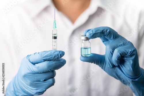 Doctor, nurse, scientist, man or women holding flu, hpv, rabies, mumps, measles, polio, or diphtheria vaccine bottle with syringe with needle prepare for immunization in baby, child or adult patient