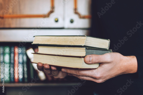 Man, Student holding many books in hands on the background of bookshelves. Male hands hold a large stack of books