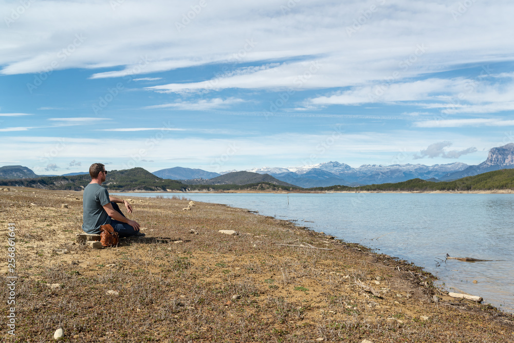 Fototapeta premium hombre joven sentado a la orilla de un lago, disfrutando del paisaje en un día primaveral.
