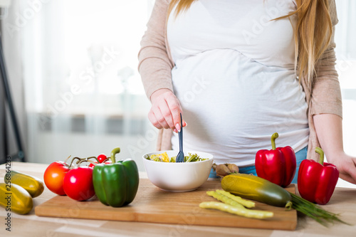 Smiling pregnant woman eating vegetables salad for health, close up