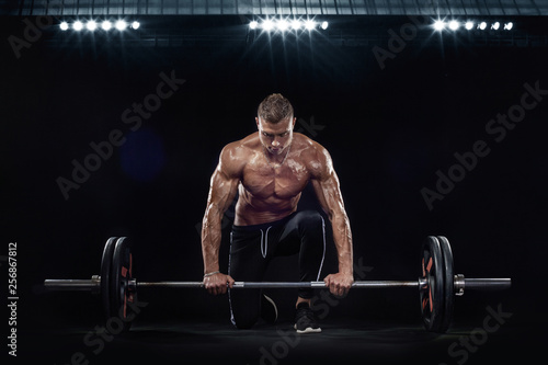 Photo of strong muscular bodybuilder athletic man pumping up muscles with barbell on black background. Workout energy bodybuilding concept.