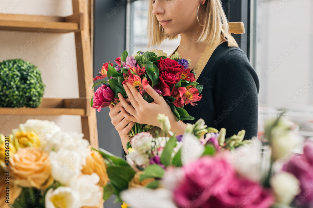 Cropped view of florist in apron holding bouquet in flower shop