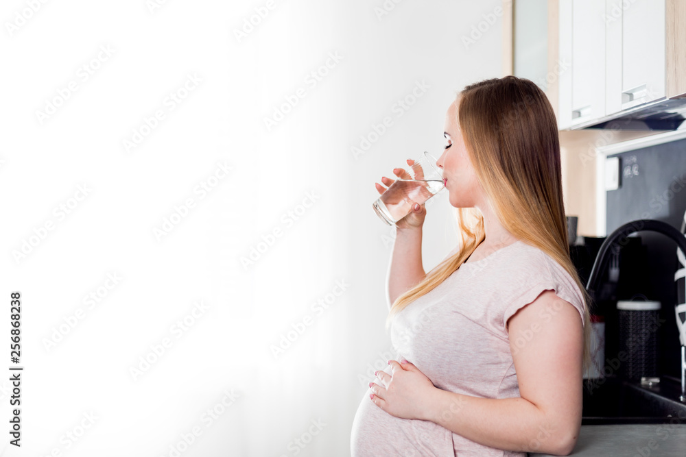 Pregnant woman drinking fresh water in kitchen, healthcare during pregnancy concept Pregnant woman drinking fresh water in kitchen, healthcare during pregnancy concept