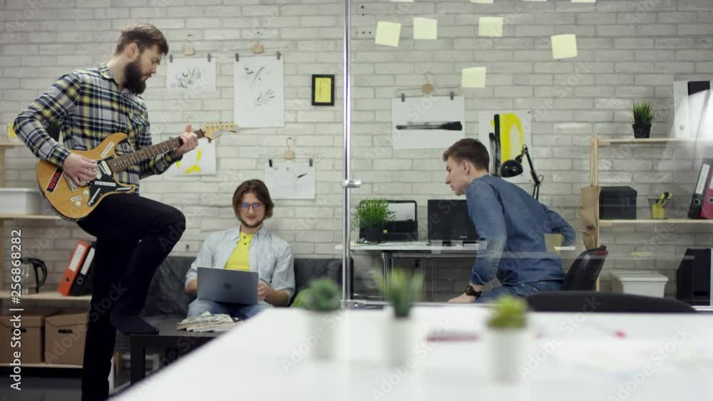 Happy successful business people in office having fun throwing documents. One man is playing the guiter. They are very tired and enjoy the coffee break.