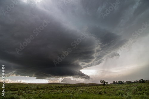 A wall cloud forms underneath a supercell storm, over fields of sagebrush.