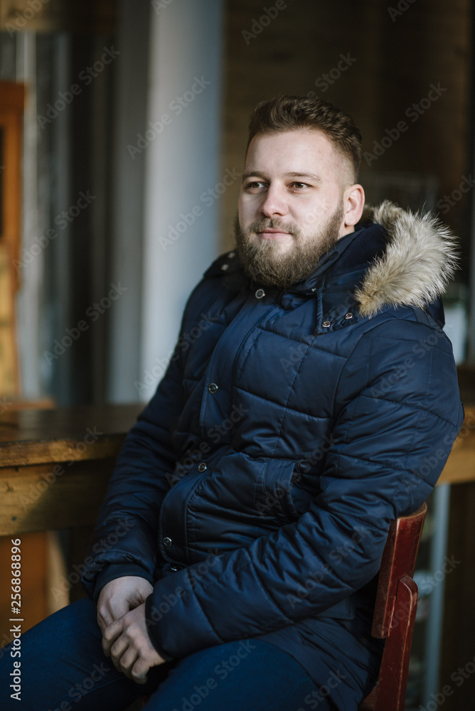 A man with a beard in a warm winter jacket poses for advertising men's clothing in the winter. Advertising of men's clothing A man with a beard in a warm winter jacket poses for advertising men's clothing in the winter. Advertising of men's clothing