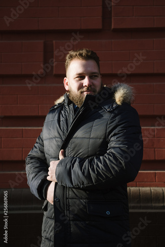 A man with a beard in a warm winter jacket poses for advertising men's clothing in the winter. Advertising of men's clothing