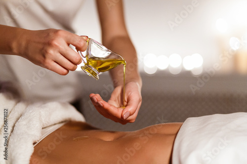 Masseur pouring oil on hand, preparing for massage photo