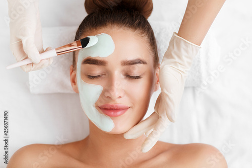 Beautician applying clay face mask on woman face