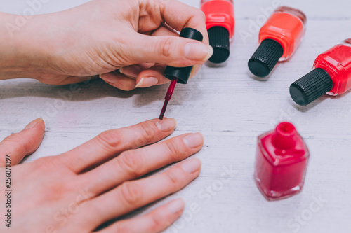 woman s hands with red nail polish bottle and other colors on wooden surface