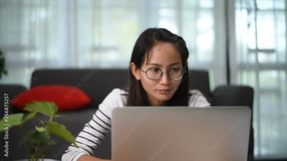 Asian woman using laptop sitting on sofa in the living room at home Asian woman using laptop sitting on sofa in the living room at home