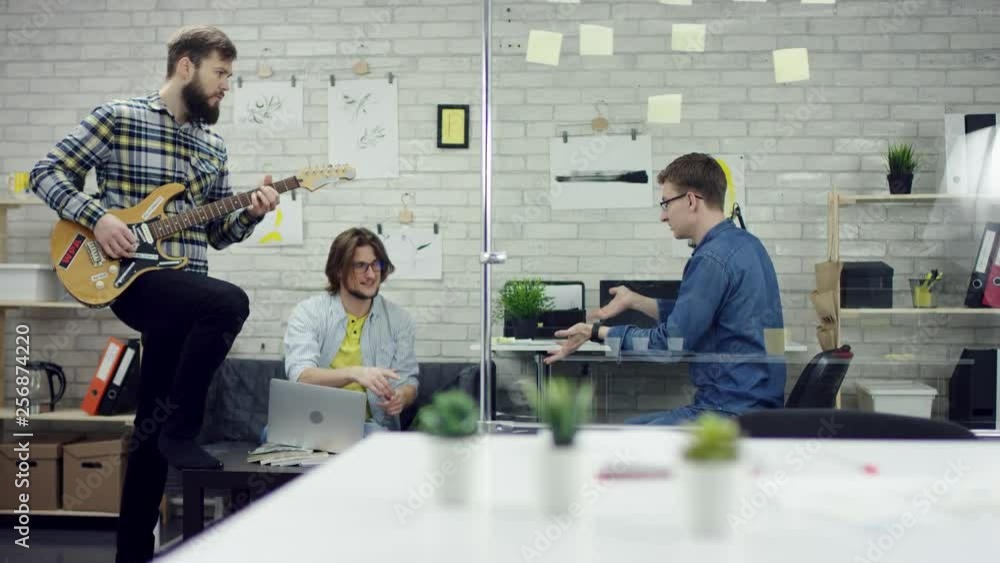 Happy successful business people in office having fun throwing documents. One worker is playing the guiter. They are very tired and enjoy the coffee break.