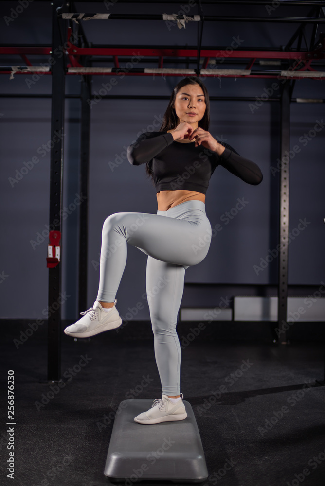 Athletic young woman using step platform in the gym. Asian blonde woman with ponytail in sportswear doing exercises on steps Athletic young woman using step platform in the gym. Asian blonde woman with ponytail in sportswear doing exercises on steps