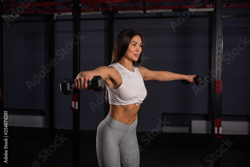 Asian woman lifting dumbbell. Young sporty muscular woman holding dumbbells