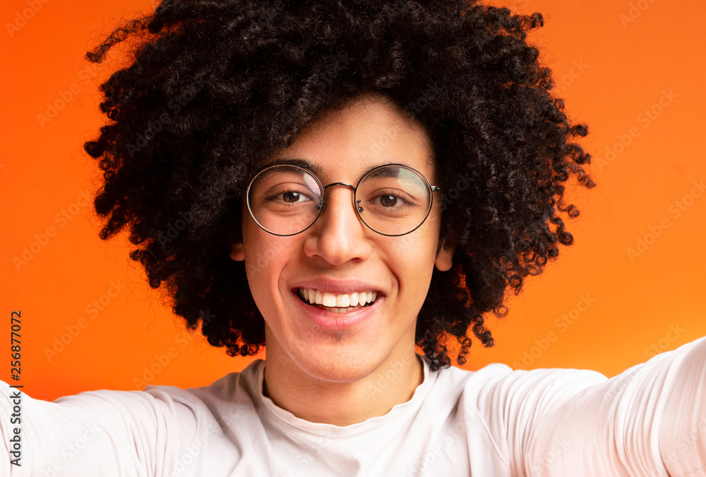 Obraz premium Cheerful millennial african-american guy making selfie on orange