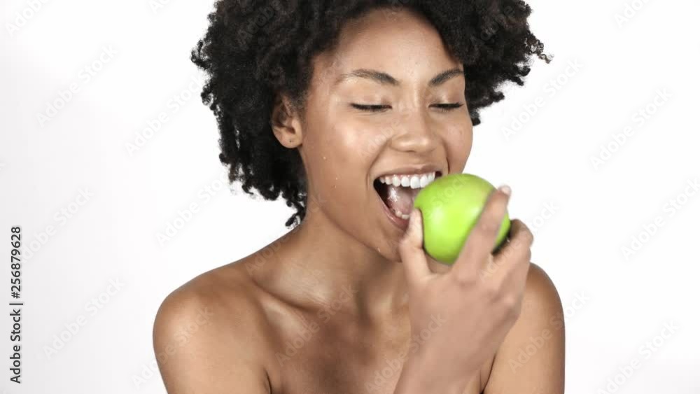 cheerful naked african american girl looking at green apple, biting, eating and laughing isolated on white cheerful naked african american girl looking at green apple, biting, eating and laughing isolated on white