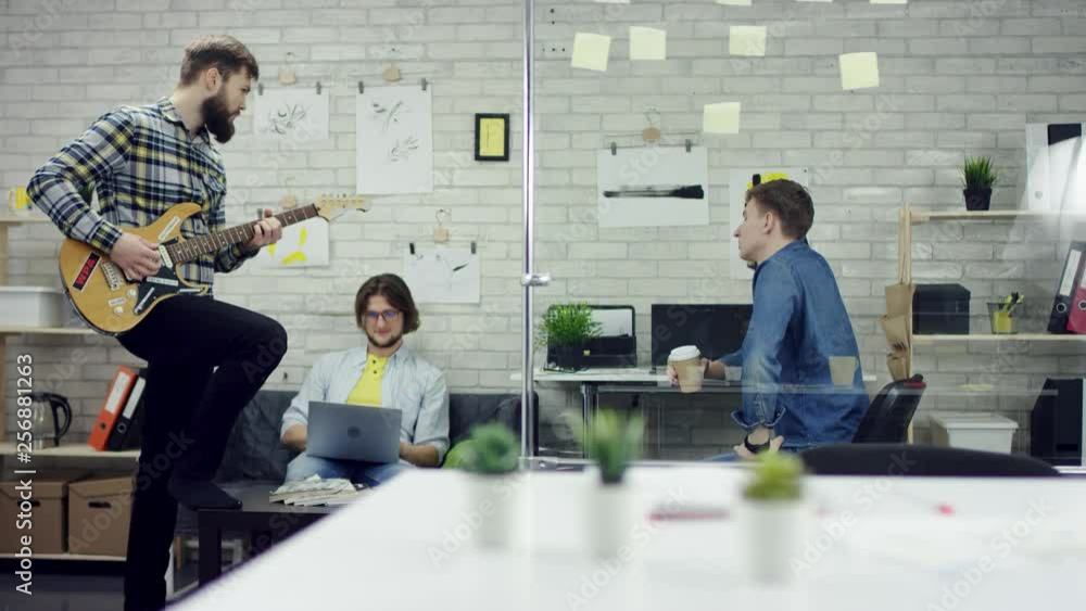 Happy successful business people in office having fun throwing documents. One man is playing the guiter. They are very tired and enjoy the coffee break. They are relaxed