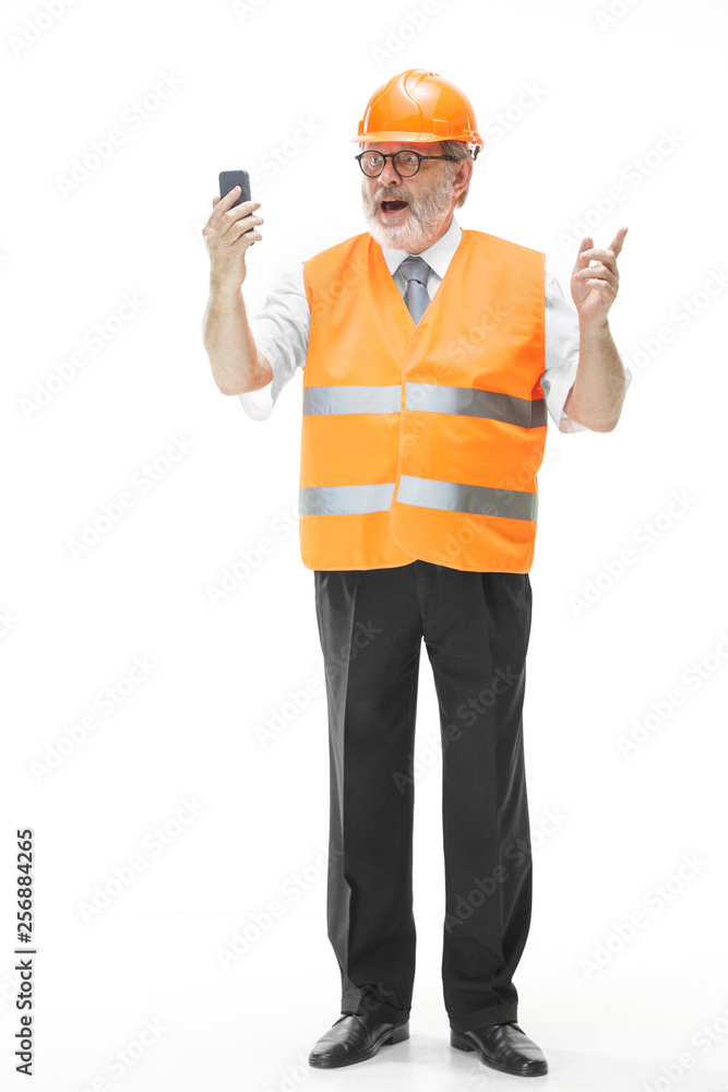 The builder in a construction vest and an orange helmet talking on a mobile phone about something. Safety specialist, engineer, industry, architecture, manager, occupation, businessman, job concept The builder in a construction vest and an orange helmet talking on a mobile phone about something. Safety specialist, engineer, industry, architecture, manager, occupation, businessman, job concept