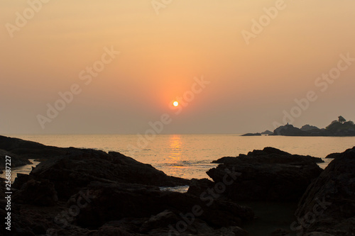 rocks in the shadows on the background of a sun path into the sea under a purple pink sunset sky