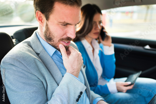 Busy attractive businessman and his assistant businesswoman sitting in a car driving to work. Modern successful businessman.