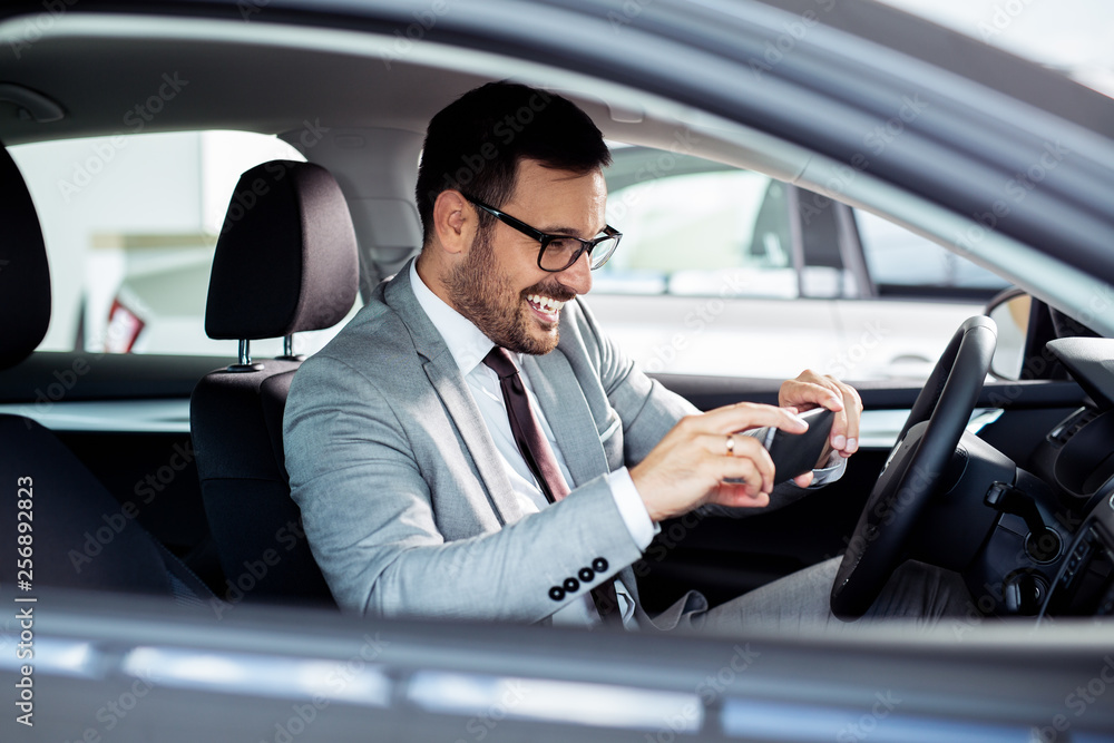 Businessman is choosing a new vehicle in car dealership and making photo on a smartphone