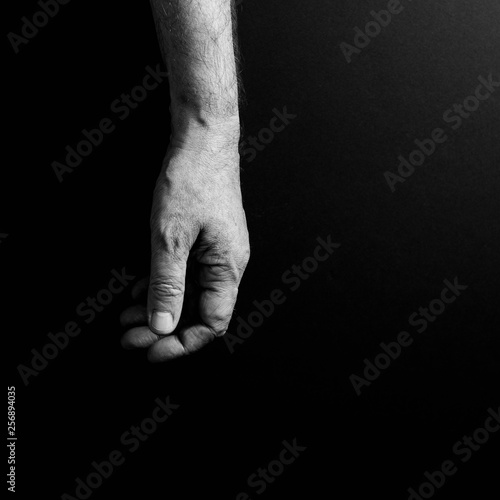 Black & white image of man's hand hanging loosely, isolated against a black background with dramatic sidelight.