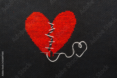 The broken heart is embroidered with red threads on a black cloth.