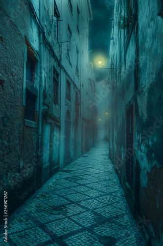  narrow old and scary street with shabby, dilapidated houses and dim lanterns in a medieval city at night