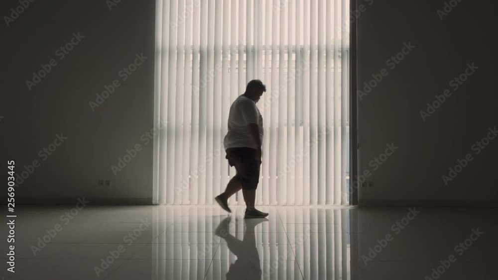 Silhouette of stressful overweight man walking near the window at home. Shot in 4k resolution Silhouette of stressful overweight man walking near the window at home. Shot in 4k resolution