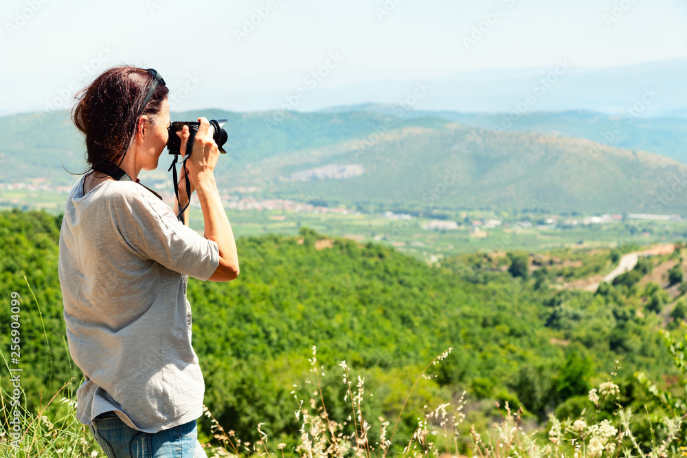 Back view of a woman photographer taking pictures of the valley with mountains from above.