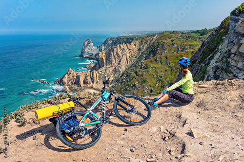 Adult attractive female cyclist  with her mountain bike sits on a ocean rocky coast.