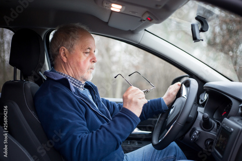 Senior man putting on glasses before driving, his eyesight is not good, safety and transportation concept