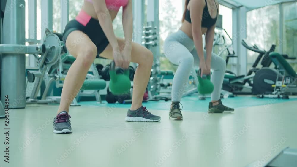 Low section of two fit young woman doing squats with weights in their hands in modern sports club Low section of two fit young woman doing squats with weights in their hands in modern sports club