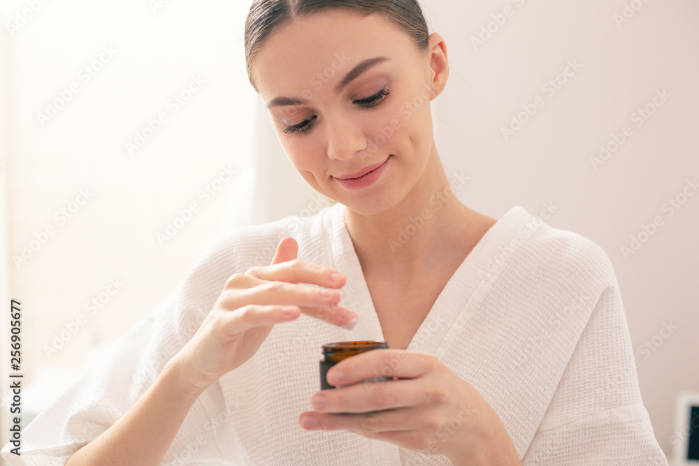 Calm lady smiling and taking cream from the little jar Calm lady smiling and taking cream from the little jar