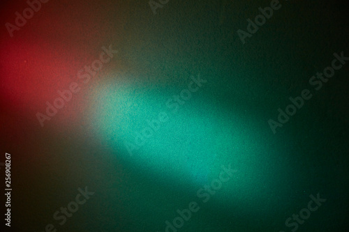 Turquoise spot of light on a dark green textural background with a red glow