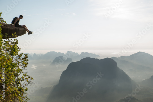 Dizziness concept: person sitting on the end of a mountain cliff looking down at the jump